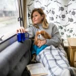 Adult woman looking out of the window with her dog and thinking about her life and future