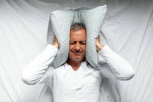 One mature man trying to sleep covering his ears to avoid neighbour noise at home or hotel during the day.