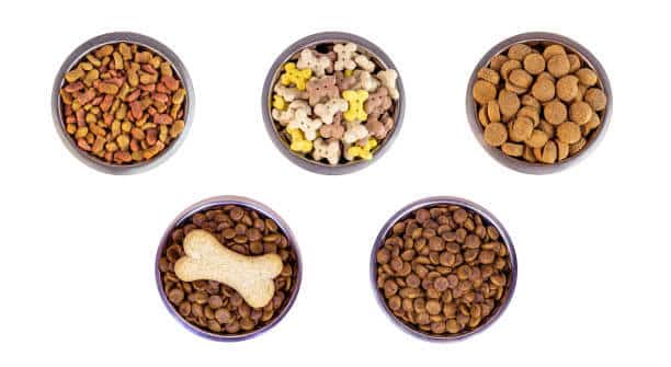 Top view of brown biscuit bones and crunchy organic kibble pieces for dog feed in a metal bowl set isolated on white background. Healthy dry pet food concept.
